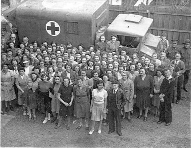 [workers standing in front of a truck converted for use as a military ambulance]